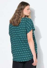 Top corto a maniche corte di colore teal con motivo a rombi. Tessuto morbido, vestibilità comoda, orlo arrotondato e sottile design sovrapposto sul retro.