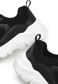 Scarpe da atletica nere con una combinazione di pelle liscia e testurizzata, suole bianche spesse e piccoli tiranti neri sul tallone.