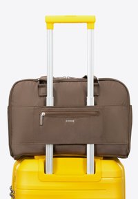 Borsa per laptop in tessuto marrone con una tasca frontale con zip, montata su una valigia gialla rigida. Sono visibili le maniglie telescopiche argentate.