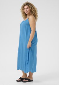 Abito lungo senza maniche di colore blu, realizzato in tessuto leggero, caratterizzato da una vestibilità comoda, pieghe sottili e un orlo dritto, abbinato a sandali neri.