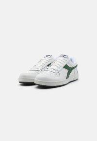 White sneaker with green accents, leather upper, perforated toe box, laces, and padded collar. Features rubber outsole and branding on tongue.