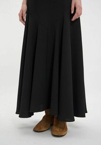 Jupe longue noire avec un ourlet évasé et des détails de couture, associée à des bottes de cheville en daim beige avec un design cousu.