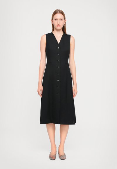 Black sleeveless dress with a V-neckline, featuring a button front, two side pockets, and a midi length design. Worn with patterned flats.