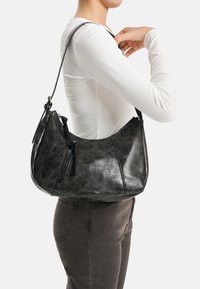 Borsa a tracolla in pelle nera con forma curva, texture stratificata e dettaglio con cerniera. La borsa è dotata di una tracolla lunga regolabile.