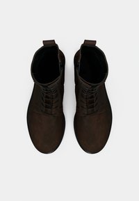 Bottes chevillage en cuir marron avec un design à lacets, bout arrondi et surface texturée. Équipées d'une languette pour un enfilage facile. Semelle en caoutchouc noire.