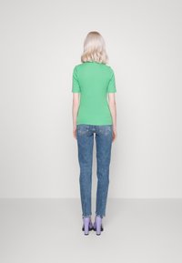 Camiseta verde de manga corta combinada con jeans ajustados azules y zapatos de tacón lavanda. Diseño sencillo con una silueta ajustada.