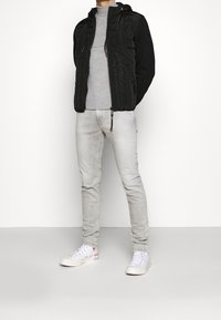 Chaqueta acolchada negra con capucha, suéter gris de cuello alto, jeans gris claro y zapatillas blancas con acentos rojos. Texturas suaves en todo.
