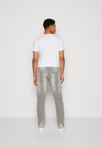 Gray denim jeans with a slim fit, faded texture, and back pockets visible. Paired with a plain white short-sleeve t-shirt.