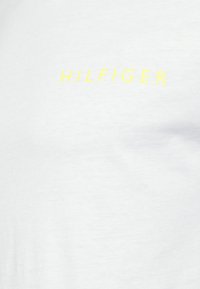 T-shirt bianca in cotone con logo "HILFIGER" in bold di colore giallo neon stampato sul petto. Texture liscia, collo giro semplice.