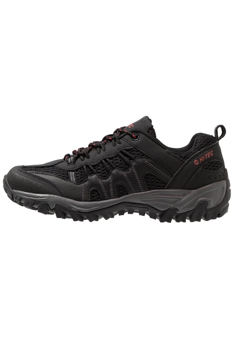Black athletic shoe made of mesh and synthetic material with a textured surface, featuring red accents, a reinforced toe, and a rugged sole.