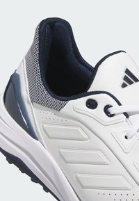 White athletic shoe with textured leather and mesh sections, featuring navy blue accents, prominent branding, and a padded collar.
