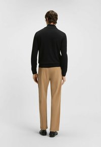 Svart stickad tröja med krage, kombinerad med beige raka byxor. Outfiten har en mjuk textur och en figurnära silhuett.