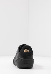 Baskets noires avec une semelle extérieure en caoutchouc texturé, une tige en cuir lisse et un accent talon en daim doux avec un écusson logo doré.