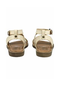 Beżowe skórzane sandały na płaskiej podeszwie, z zapięciem na kostkę zabezpieczonym regulowanymi klamrami oraz gładką podeszwą o drewnianej fakturze.