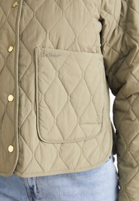 Töltött dzseki világoszöld anyagból, arany patentgombokkal, nagy, "Barbour" logós zsebbel és rövidített fazonnal.