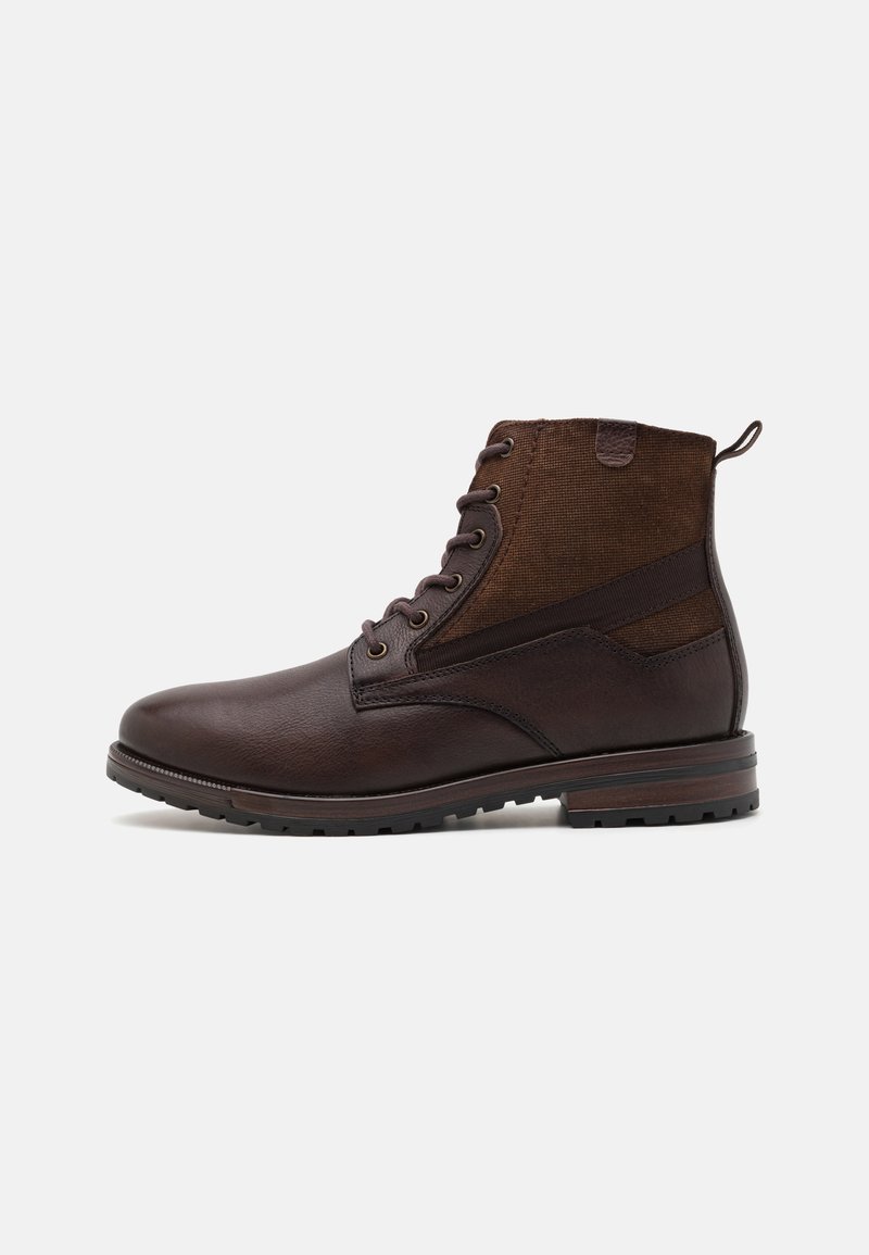 Botas de tobillo de cuero marrón con paneles laterales de lona, puntera redonda y diseño con cordones. Presenta un acabado texturizado y suelas de goma para tracción.