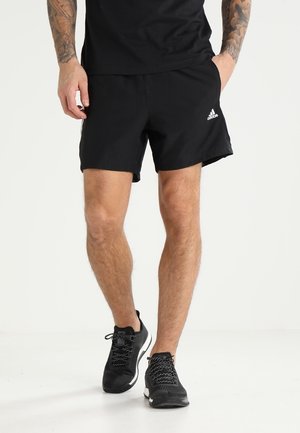 Czarne sportowe szorty wykonane z lekkiego materiału, z elastycznym paskiem w talii i logo Adidas po boku, w zestawieniu z czarnymi sneakersami.