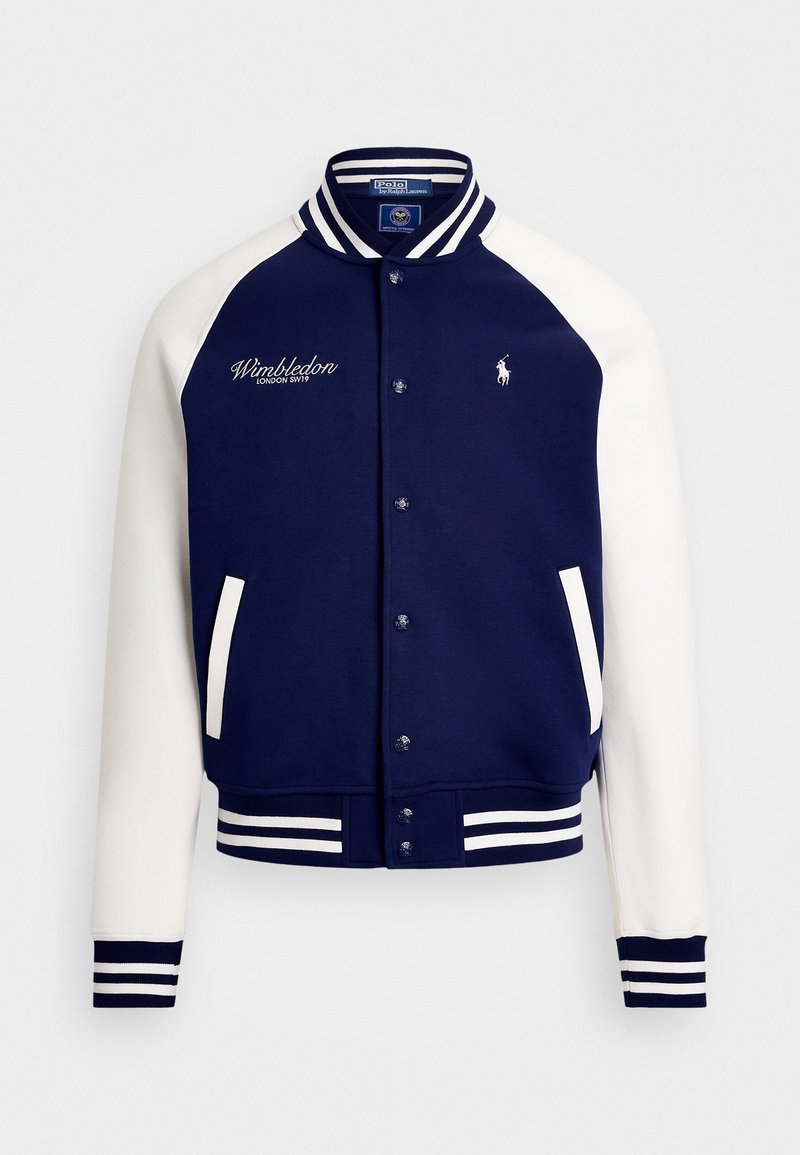 Veste bomber bleu marine avec manches blanches, poignets et ceinture côtelés. Elle arbore une broderie "Wimbledon" et un petit logo sur la poitrine.