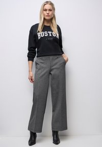 Czarna bluza z nadrukiem "BOSTON 1980", w połączeniu z szarymi spodniami o szerokich nogawkach i czarnymi botkami za kostkę. Teksturowany materiał spodni, casualowy styl.