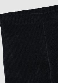 Tessuto in velluto a coste nero, che mostra una texture rigata verticale. Primo piano del bordo della cintura con una finitura morbida e dettagli di cucitura puliti e dritti.