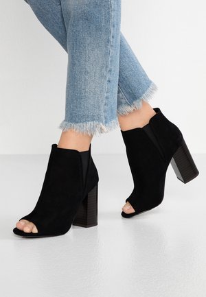 Sorte ruskind åbne ankelsko med chunky hæl og elastiske sidespaneler, kombineret med cropped frayed blå denimjeans.