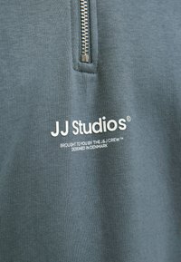 Tessuto blu con cerniera verticale sopra il testo bianco che recita "JJ Studios, presentato dal team J&J, progettato in Danimarca."