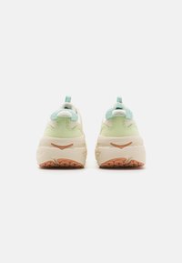 Sneakers robustos com um superior em verde pálido e branco, realces texturizados e uma sola grossa em creme com uma resistência em castanho claro.