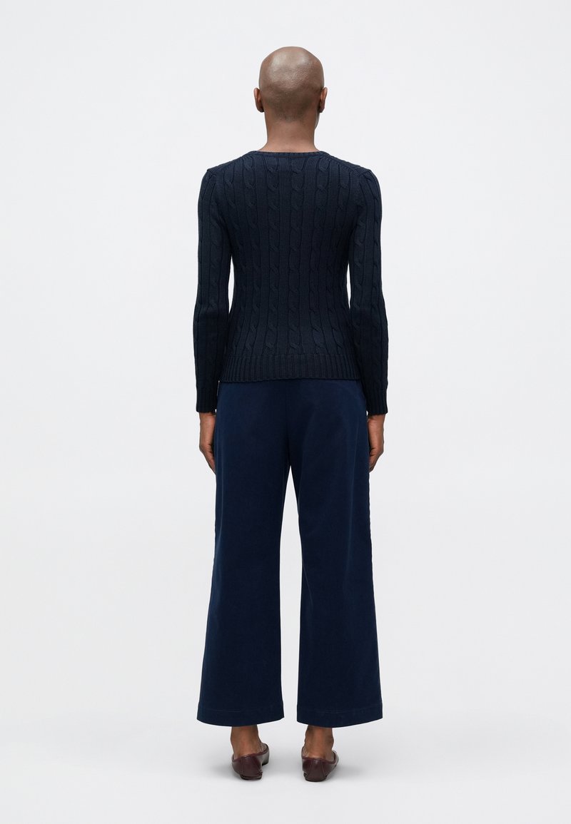 Pull en tricot côtelé marine à manches longues, associé à un pantalon large marine et des chaussures brunes. Mettez l'accent sur le motif texturé en tricot et l'ajustement.