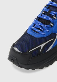 Chaussure de sport bleue et noire avec une tige en mesh, tissu texturé, accents réfléchissants et une semelle en caoutchouc robuste. Dispose de lacets ronds et d'un col rembourré.