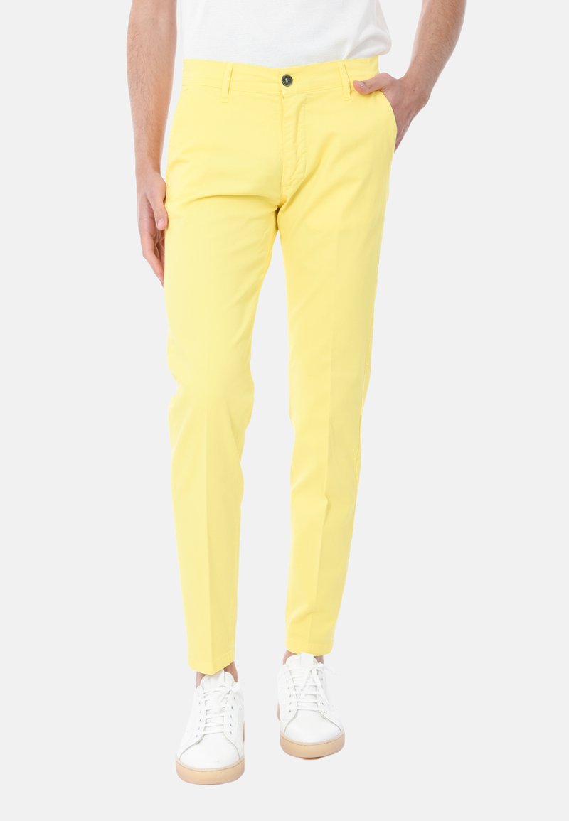 Chino gialli in cotone con una vestibilità slim, caratterizzati da tasche laterali, chiusura con bottone anteriore e abbinati a sneakers bianche.