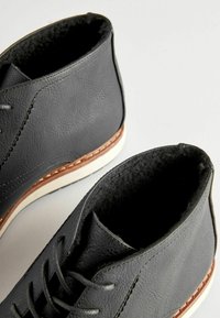 Botas de tobillo de cuero gris con un acabado texturizado, suelas de goma blanca, detalles en beige y cordones grises. Incluyen un forro de tela suave.