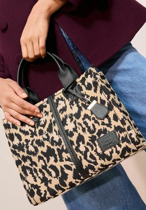 Sac fourre-tout en tissu beige et noir à motif léopard, doté de poignées en cuir noir et d'une fermeture éclair contrastante avec une étiquette attachée.