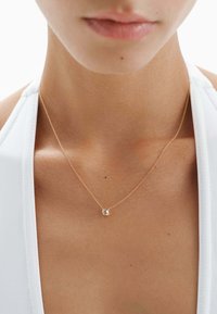 Collar de cadena de oro con un pequeño colgante redondo que presenta una piedra preciosa transparente, reposando sobre piel desnuda. Diseño sencillo, apariencia delicada.