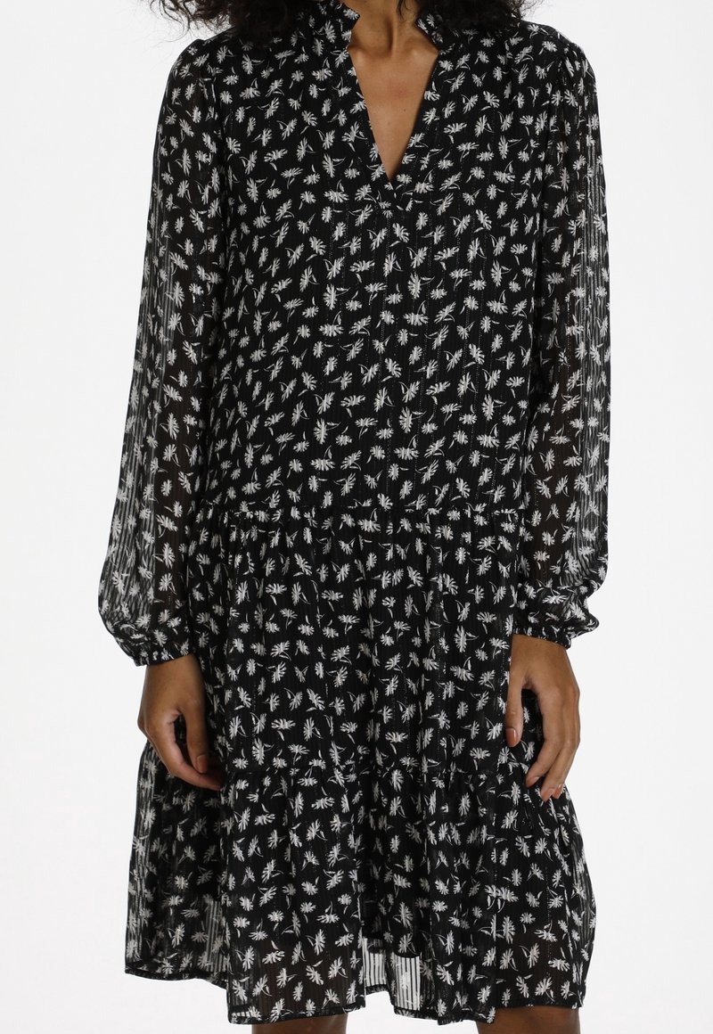 Svart klänning med ett blommigt vitt mönster, långa genomskinliga ärmar med elastiska manschetter, och en flikig kjoldesign.