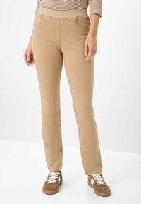 Beige broek met een rekbare tailleband, slim fit, voorzakken en een gladde textuur. Combinatie met bruine sneakers met witte veters.