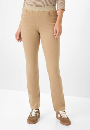 Beige Hosen mit einem dehnbaren Bund, schmaler Passform, Vorderentaschen und glatter Textur. Kombiniert mit braunen Sneakers mit weißen Schnürsenkeln.