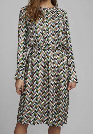 Mujer con un vestido con cinturón y mangas largas con un patrón de chevron vertical multicolor en negro, azul, verde, rosa y blanco.