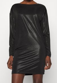 Svart långärmad klänning i glittrande tyg, med en lösa passform, båtformad halsringning och rynkad textur längs midjan.