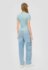 Top corto a maniche corte di colore blu chiaro con una scollatura arrotondata. Abbinato a jeans cargo in denim chiaro, che mostrano dettagli delle tasche e una vestibilità rilassata.