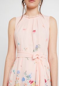 Blumenmuster, ärmelloses Kleid aus leichtem, pinkfarbenem Stoff. Mit einem rüschierten Ausschnitt und einem gebundenen Taillengürtel mit bunten Blumenmustern.