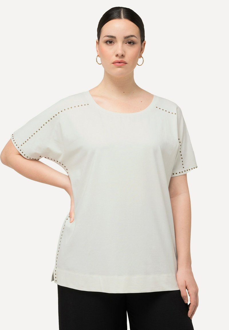 Camiseta blanca de manga corta con acentos laterales de tachuelas doradas, cuello redondo y un corte relajado. Fabricada en un tejido ligero.