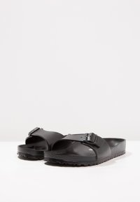 Sandale negre cu slip-on din material sintetic texturat. Prezintă o curea lată cu detaliu de cataramă, design cu vârf deschis și talpă din cauciuc.