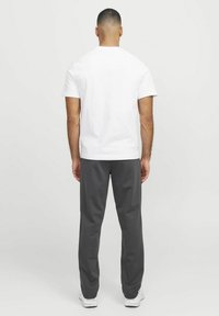 Camiseta blanca de manga corta, corte relajado, combinada con pantalones de chándal grises, bolsillos frontales y cinturilla elástica. Diseño simple y casual.