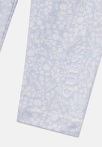 Világoskék szövet leggings, fehér virágmintával és kontrasztos fehér "GUESS" logóval az oldalon. Sima textúra.