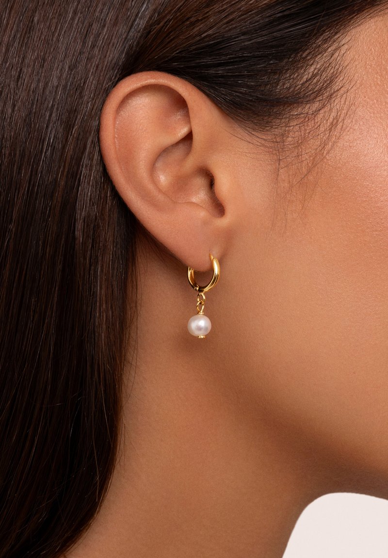 Boucles d'oreilles en or en forme de hoop avec une goutte de perle, présentant une finition brillante et une texture lisse, suspendues à un petit lien en or.