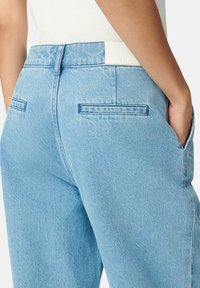 Jeans in denim azzurro chiaro con vita alta, tasche posteriori e una texture liscia, dotati di un'etichetta bianca pulita alla vita.