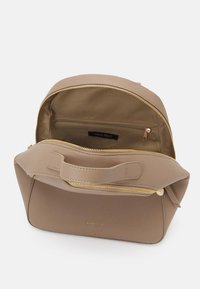 Beige laukkua, jossa on jämäkkä muoto, kultainen vetoketju, etutasku ja merkkilabel sisällä. Sileä pinta ja lyhyt kahva.
