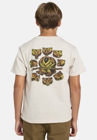 Lyhythihainen, kermaisen värinen t-paita, jossa on mustalla ja keltaisella tyyliteltyjen karhujen grafiikka selässä.