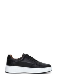 Zapatillas de piel negra con punta redonda, suela de goma blanca y costuras en contraste. Presentan cordones negros y una textura suave.