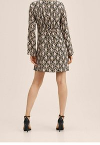 Kaavion mekko, jossa on pitkät hihat, kapea vyötärö ja pyöreä pääntie. Suunnittelussa on monimutkaisia kukkakoristeita beigeä ja vaaleanpunaista mustalla taustalla.